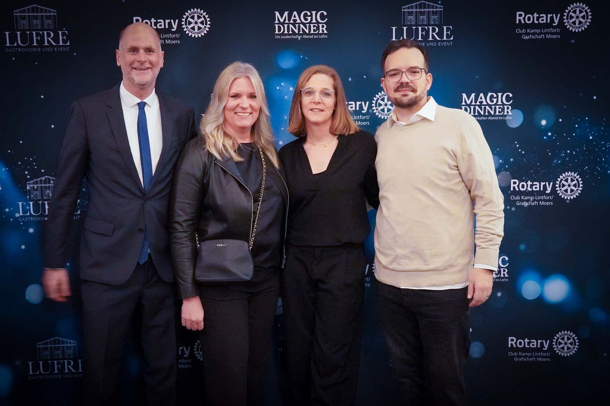 Vier Gäste in eleganter dunkler Kleidung stehen lächelnd vor der Pressewand mit Rotary- und LUFRE-Logos.