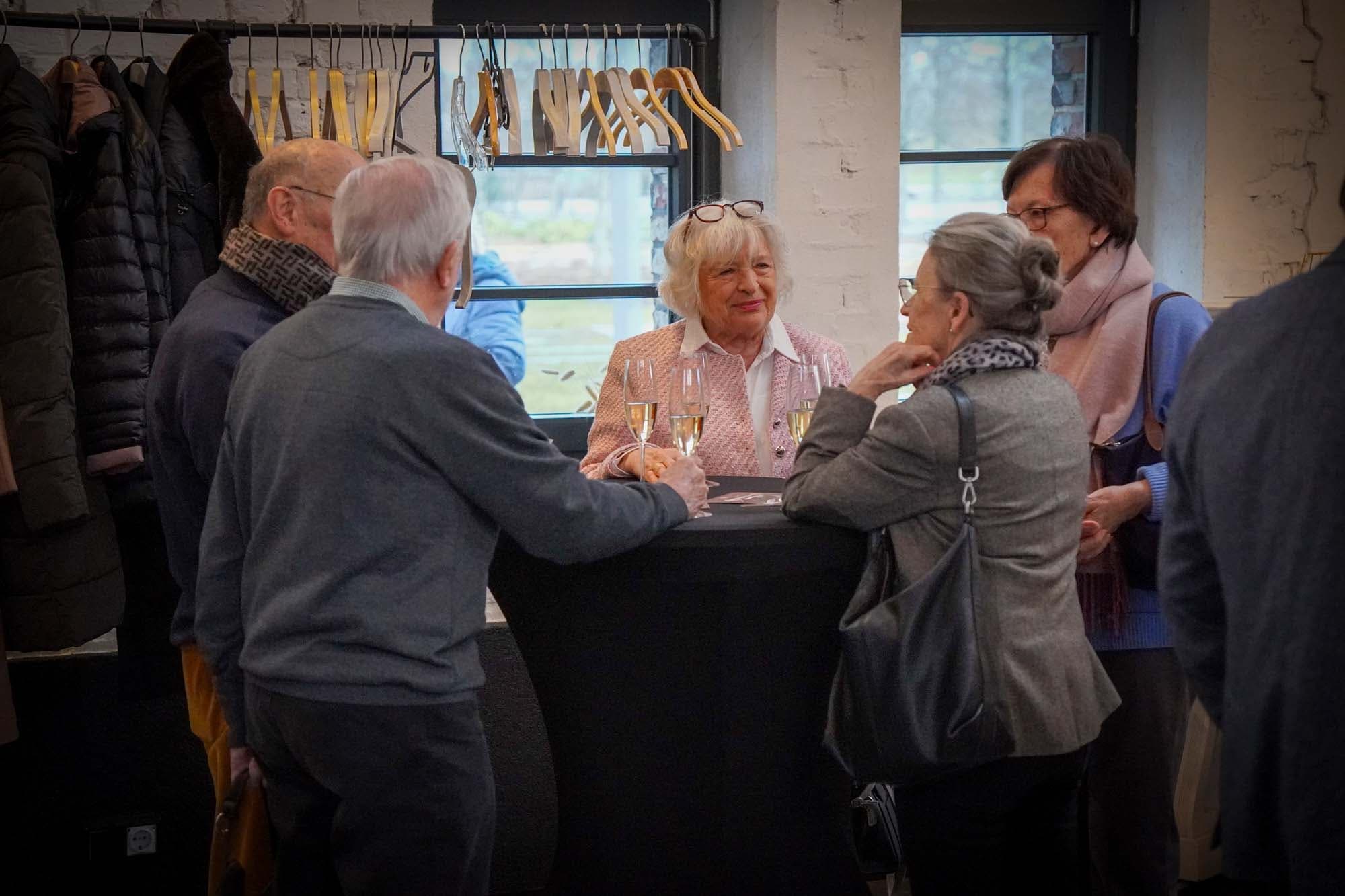 Eine Gruppe von Gästen steht mit Sektgläsern an einem Stehtisch und unterhält sich.