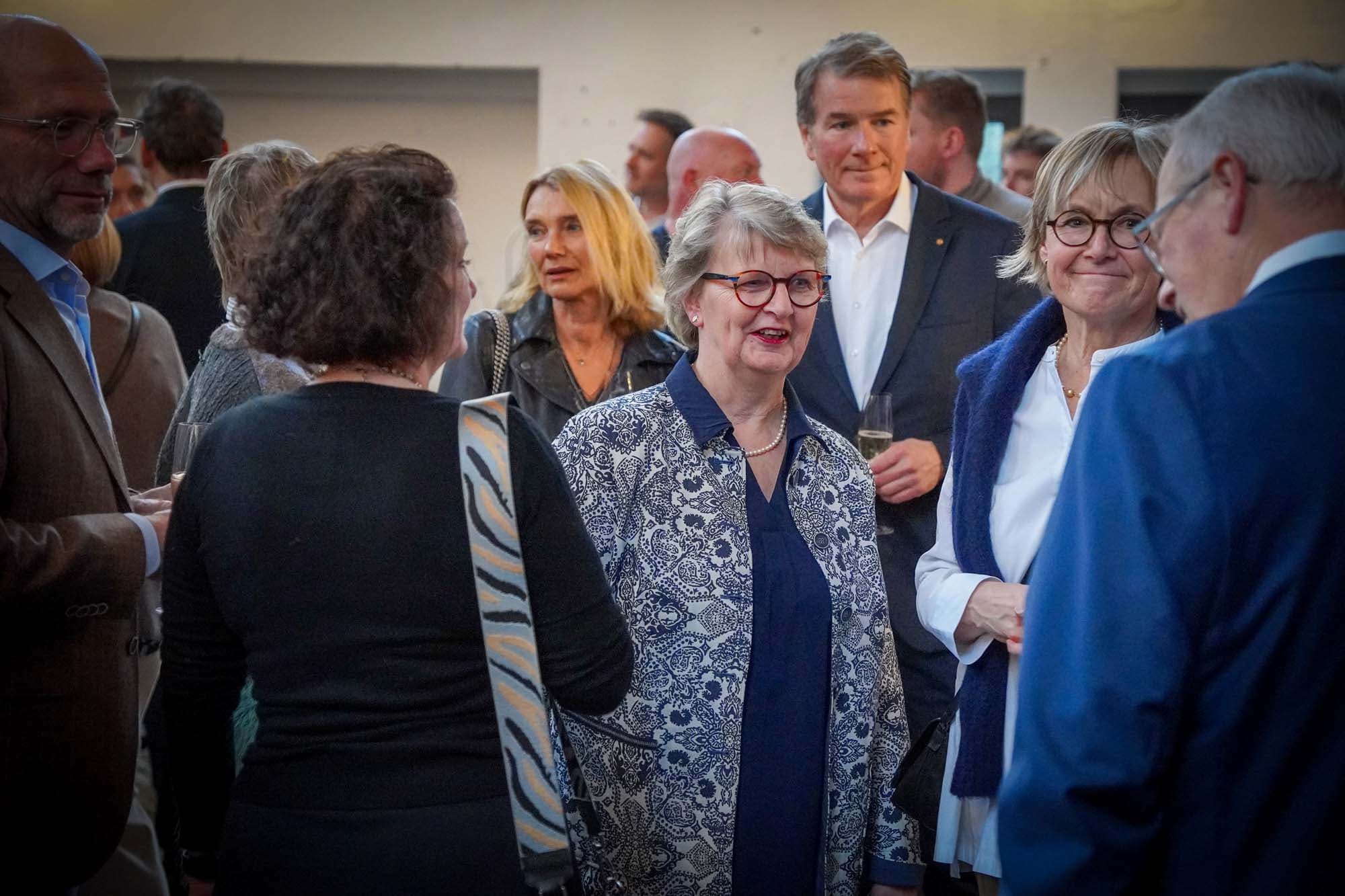 Mehrere Gäste stehen im Empfangsbereich zusammen und unterhalten sich bei einem Glas Sekt.