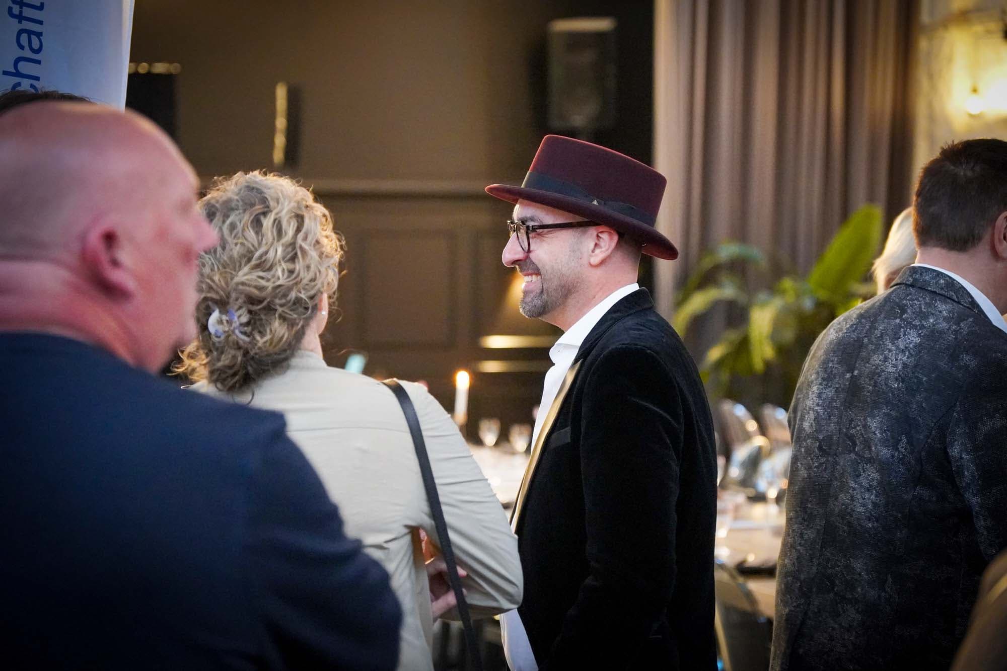 Der Zauberkünstler mit Zylinder unterhält sich lachend mit Gästen im Saal.