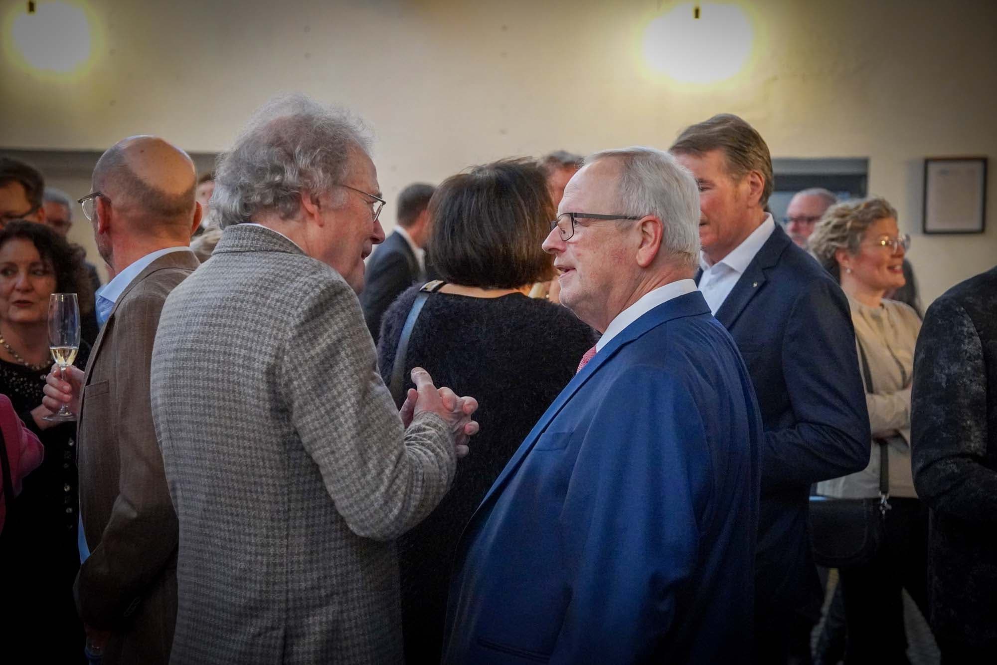 Zwei Herren im Gespräch, umgeben von weiteren Gästen beim Empfang.