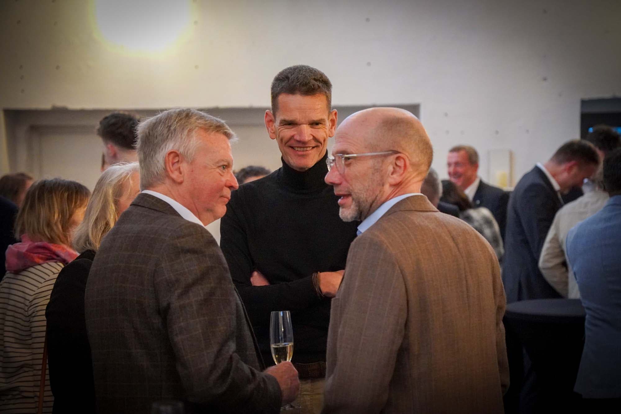 Drei Herren stehen beim Empfang zusammen und unterhalten sich in entspannter Atmosphäre.
